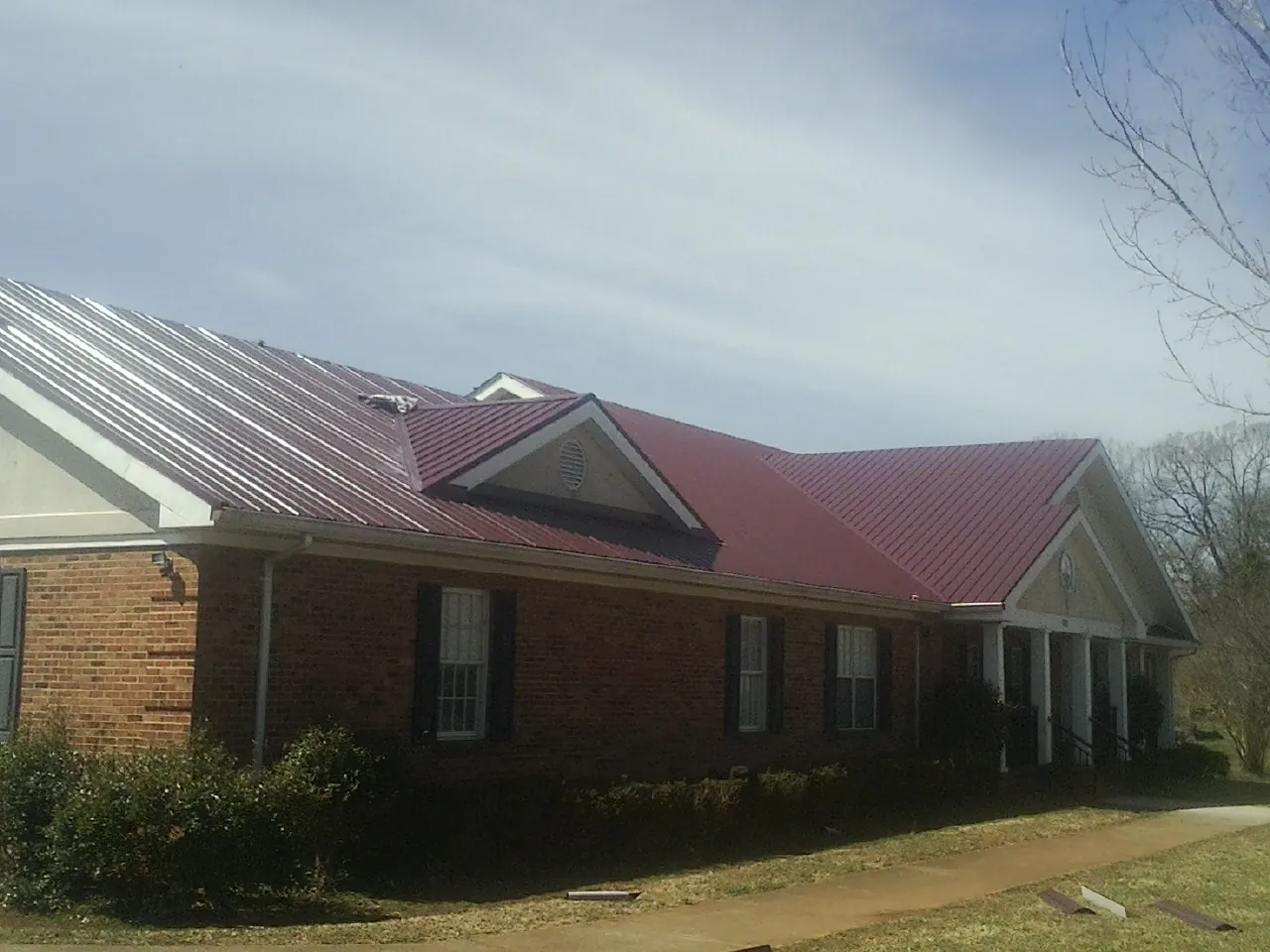 Red metal roof with gabled entries on a long brick building, from a Hail Damage Roof Repair job in Herriman
