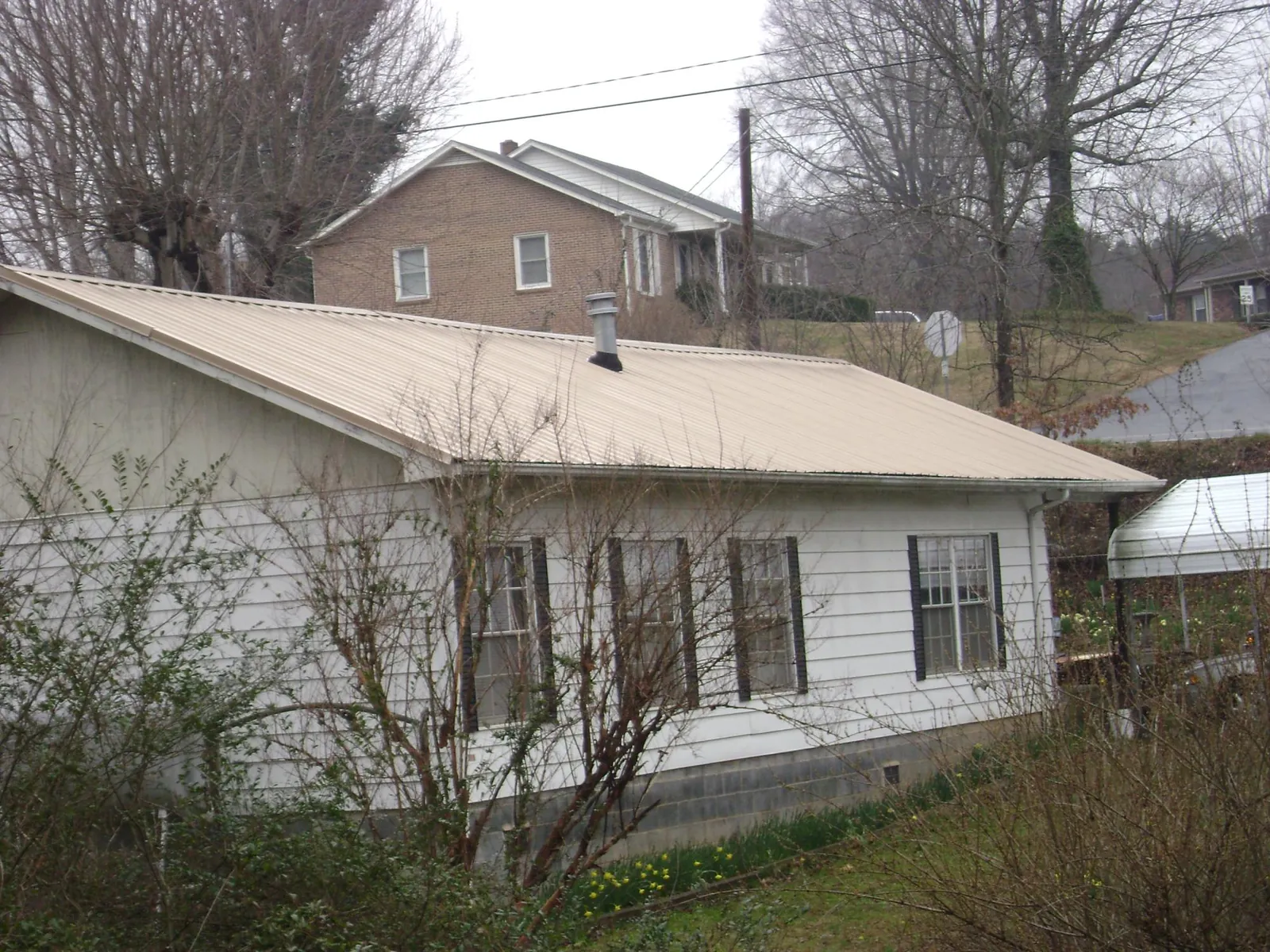 Tan metal roof on a white sided house set into a hillside in Herriman
