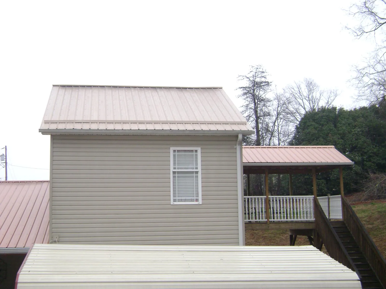 Tan metal roofs on a two story addition and attached porch, from a Roof Replacement job in Herriman